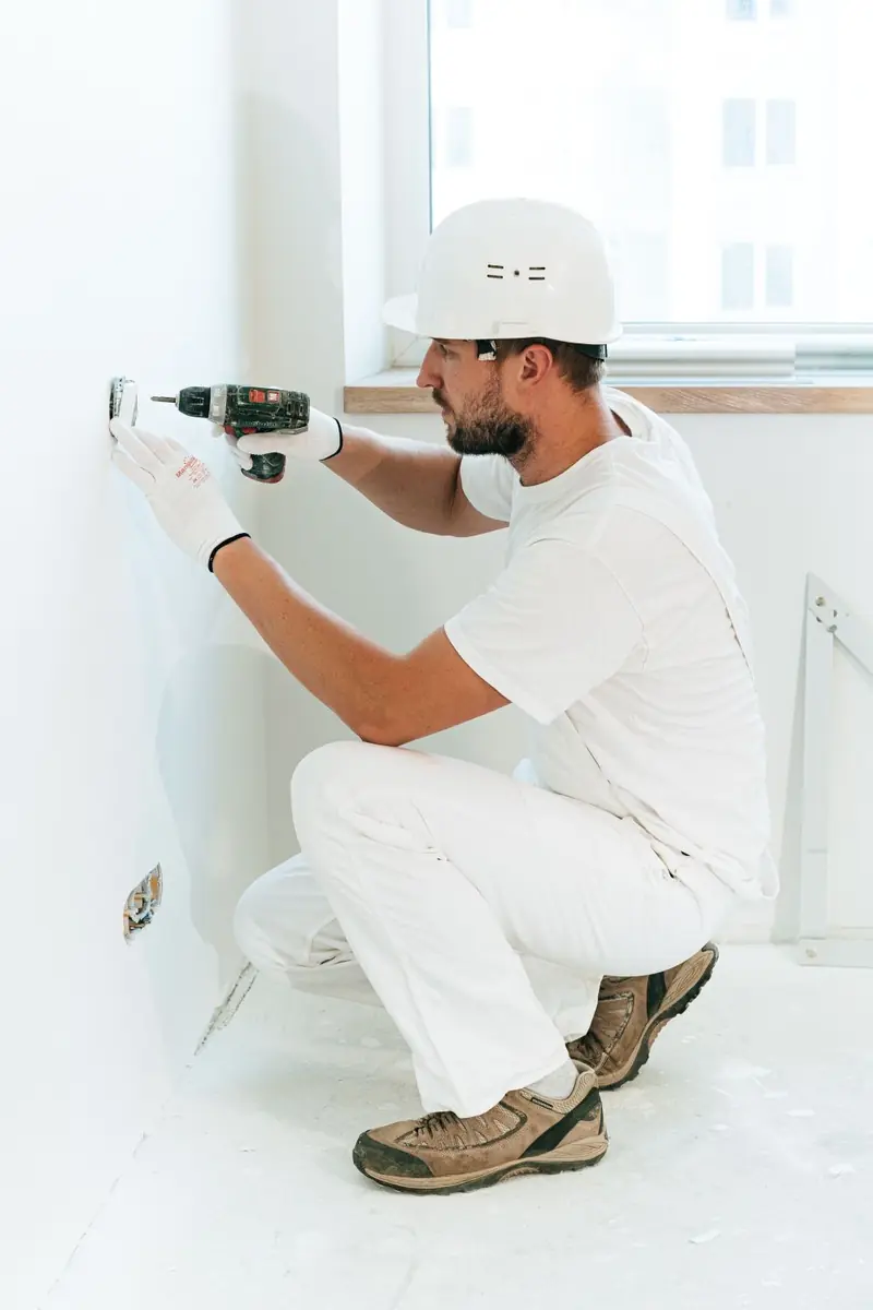 Emergency garage door technician in a hard hat repairing a door fitting in Fall River, MA